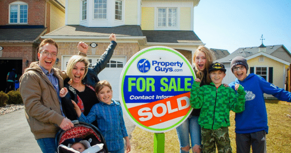 Family happily celebrating the sale of their home in front of a PropertyGuys.com “Sold” sign.