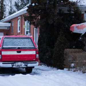 Canadian flag, snowy driveway, red SUV, brick house